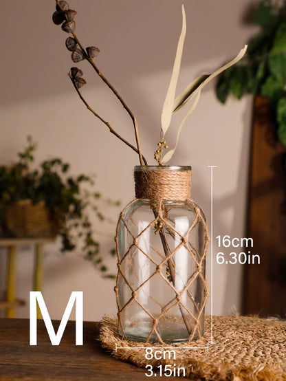 A hand‑woven hemp rope glass vase — a clear glass vessel wrapped in natural hemp fiber. Perfect for dried flowers, it adds texture and warm, rustic charm. Ideal for boho, Nordic, or minimalist interiors.