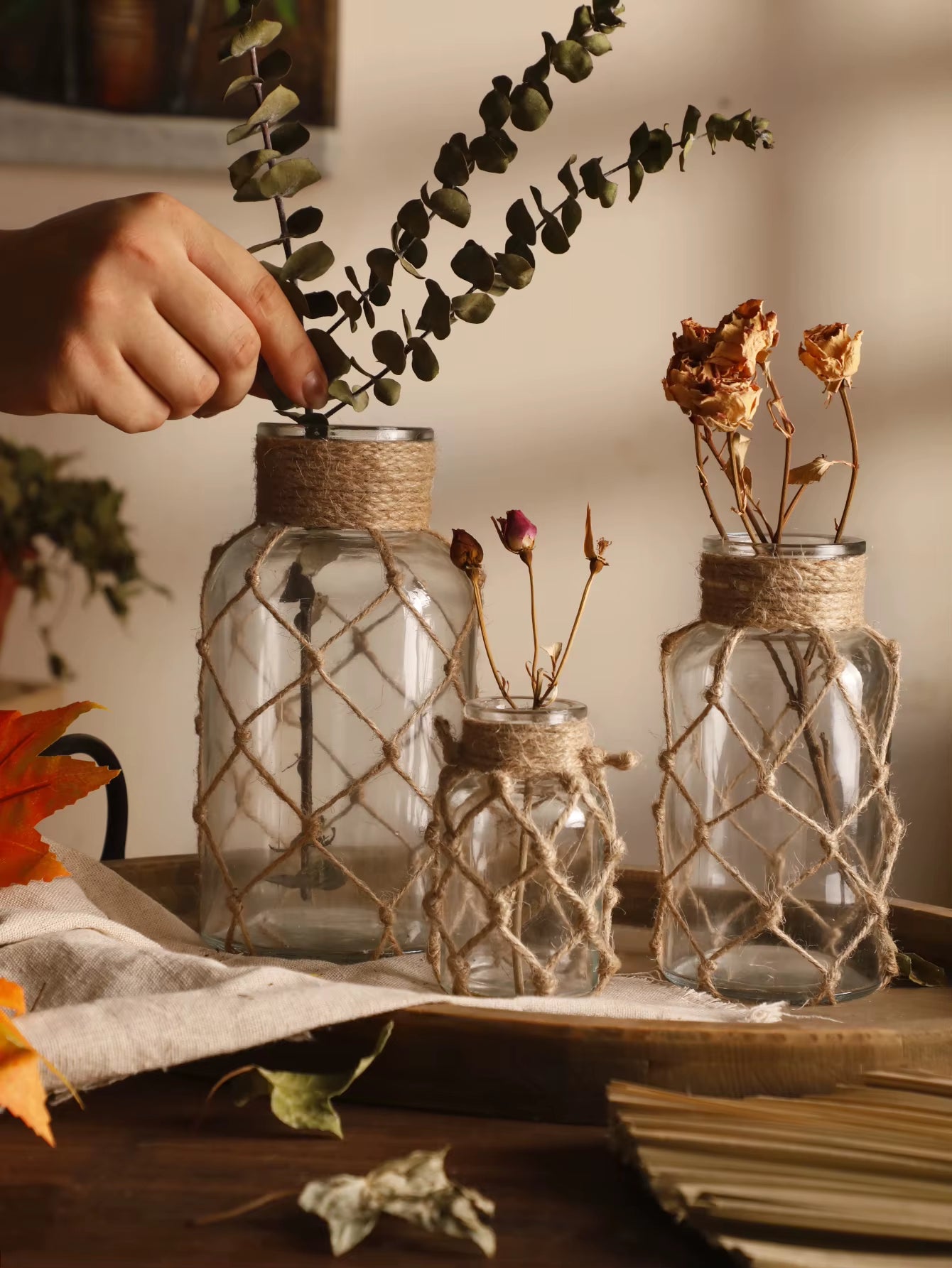 A hand‑woven hemp rope glass vase — a clear glass vessel wrapped in natural hemp fiber. Perfect for dried flowers, it adds texture and warm, rustic charm. Ideal for boho, Nordic, or minimalist interiors.