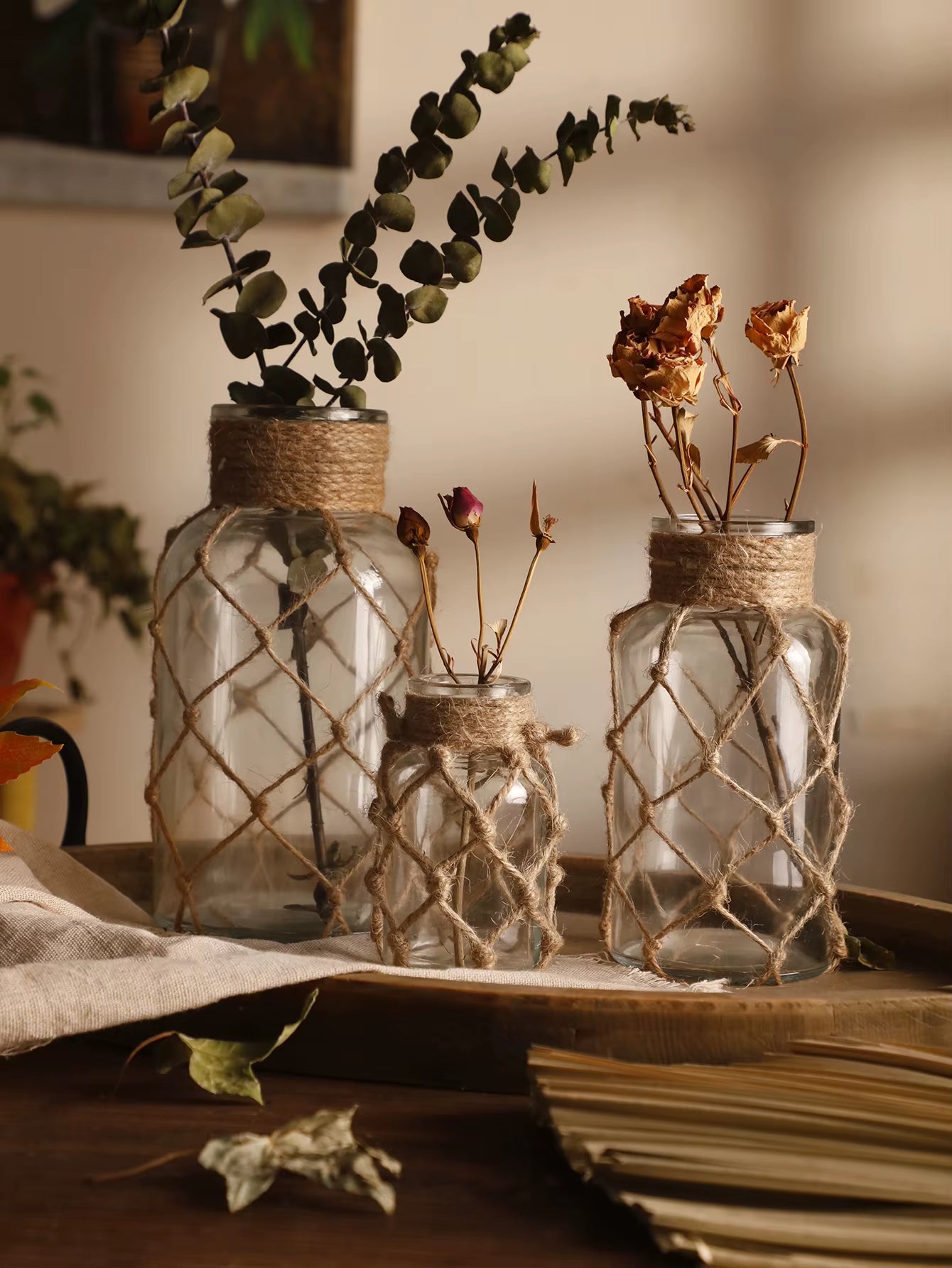 A hand‑woven hemp rope glass vase — a clear glass vessel wrapped in natural hemp fiber. Perfect for dried flowers, it adds texture and warm, rustic charm. Ideal for boho, Nordic, or minimalist interiors.