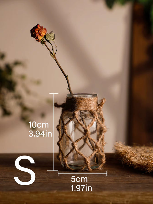 A hand‑woven hemp rope glass vase — a clear glass vessel wrapped in natural hemp fiber. Perfect for dried flowers, it adds texture and warm, rustic charm. Ideal for boho, Nordic, or minimalist interiors.